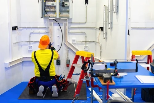 an electrician performing electrical wiring work, likely in a workshop, shed, or industrial setting